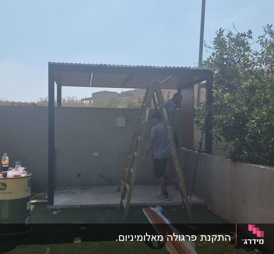 עובדים במהלך התקנת פרגולת אלומיניום עם לוחות דמוי עץ בחצר